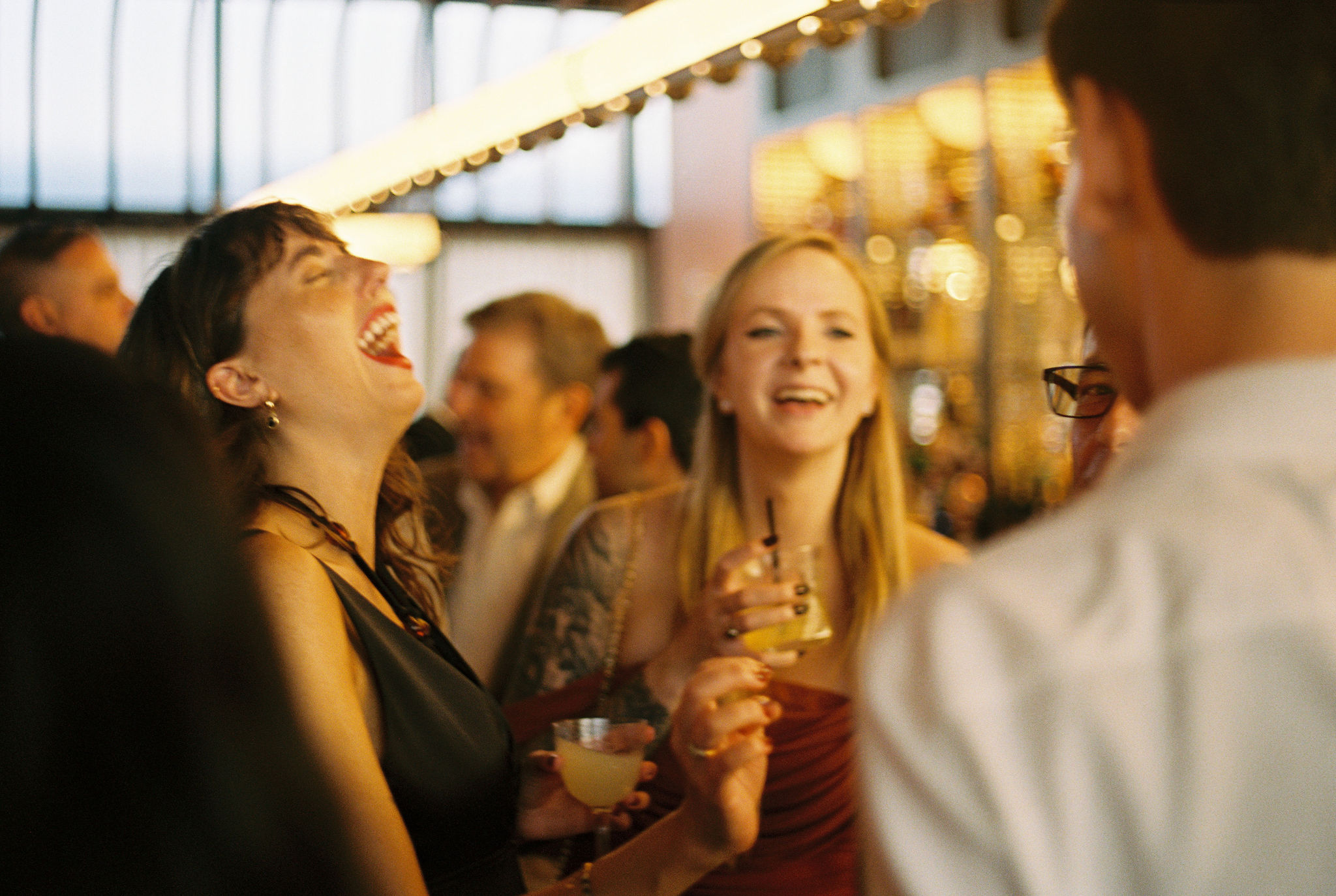 Wedding guests laughing together over cocktails at a warmly lit reception venue