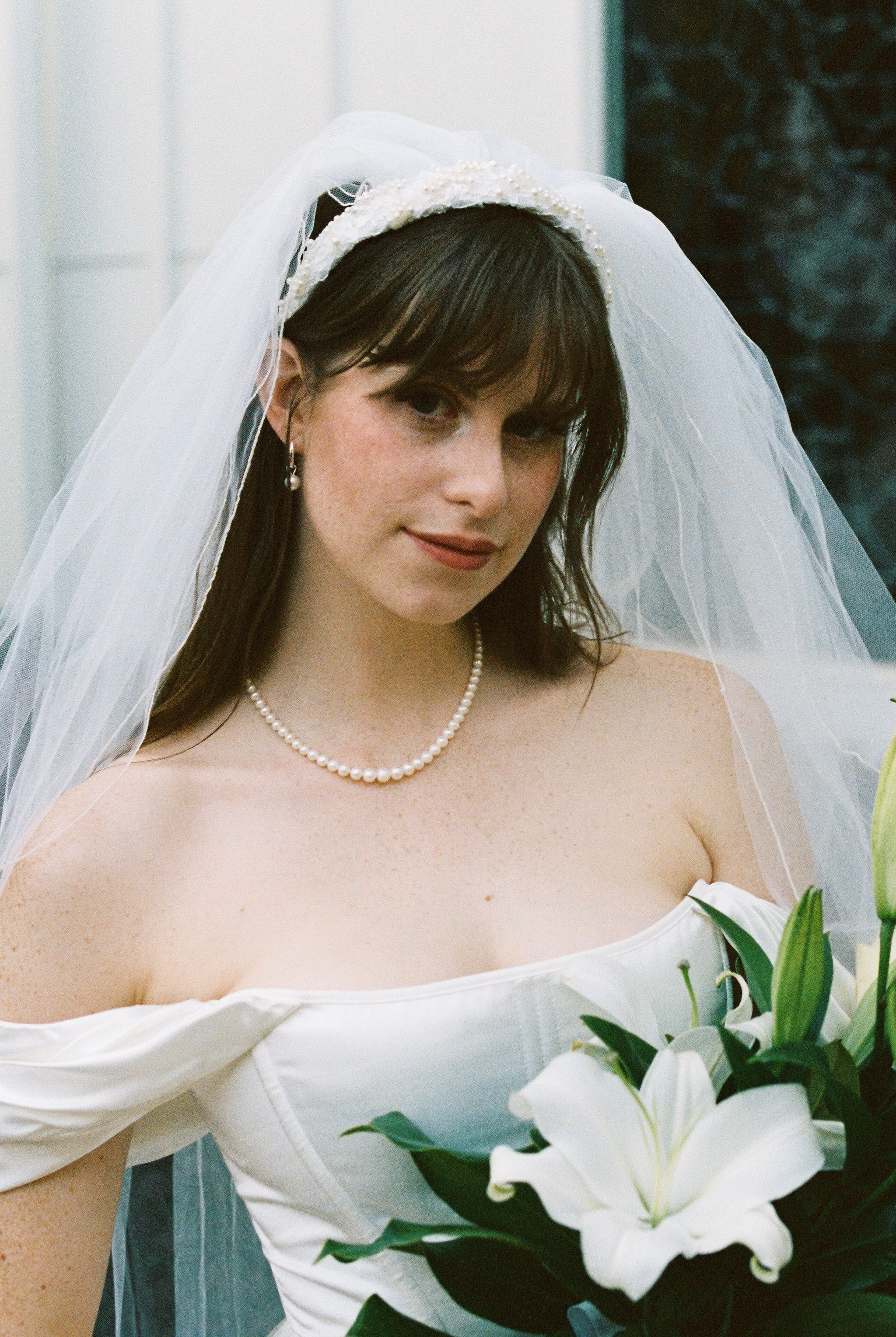 Bride portrait in veil and pearl necklace holding white lily bouquet