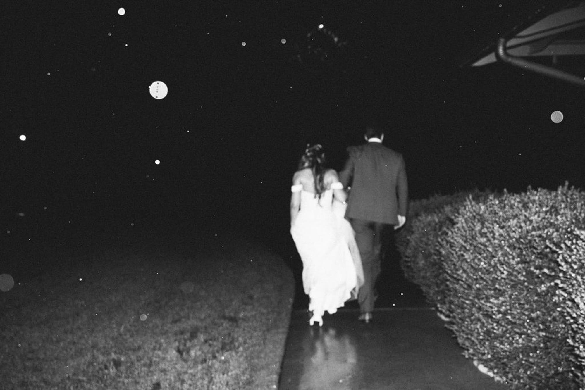 Bride and groom walking away together on a garden path at night, black and white