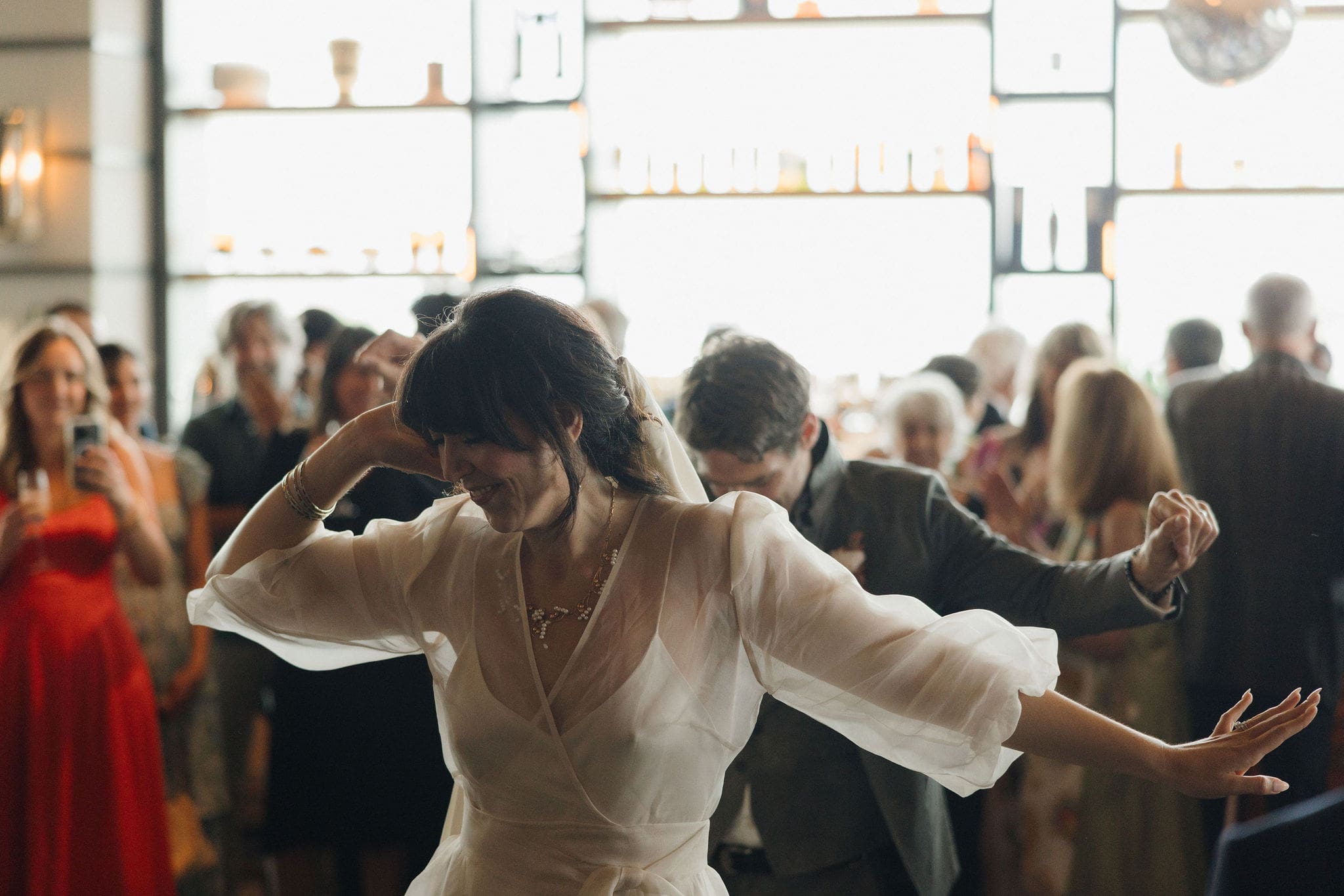 Bride dancing joyfully at wedding reception with guests in the background