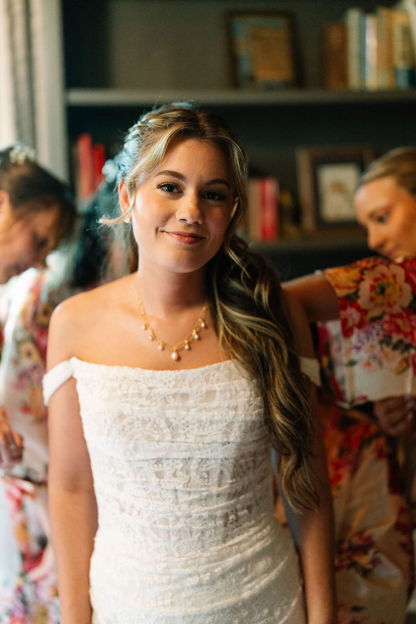 Bride smiling warmly while bridesmaids help her get ready