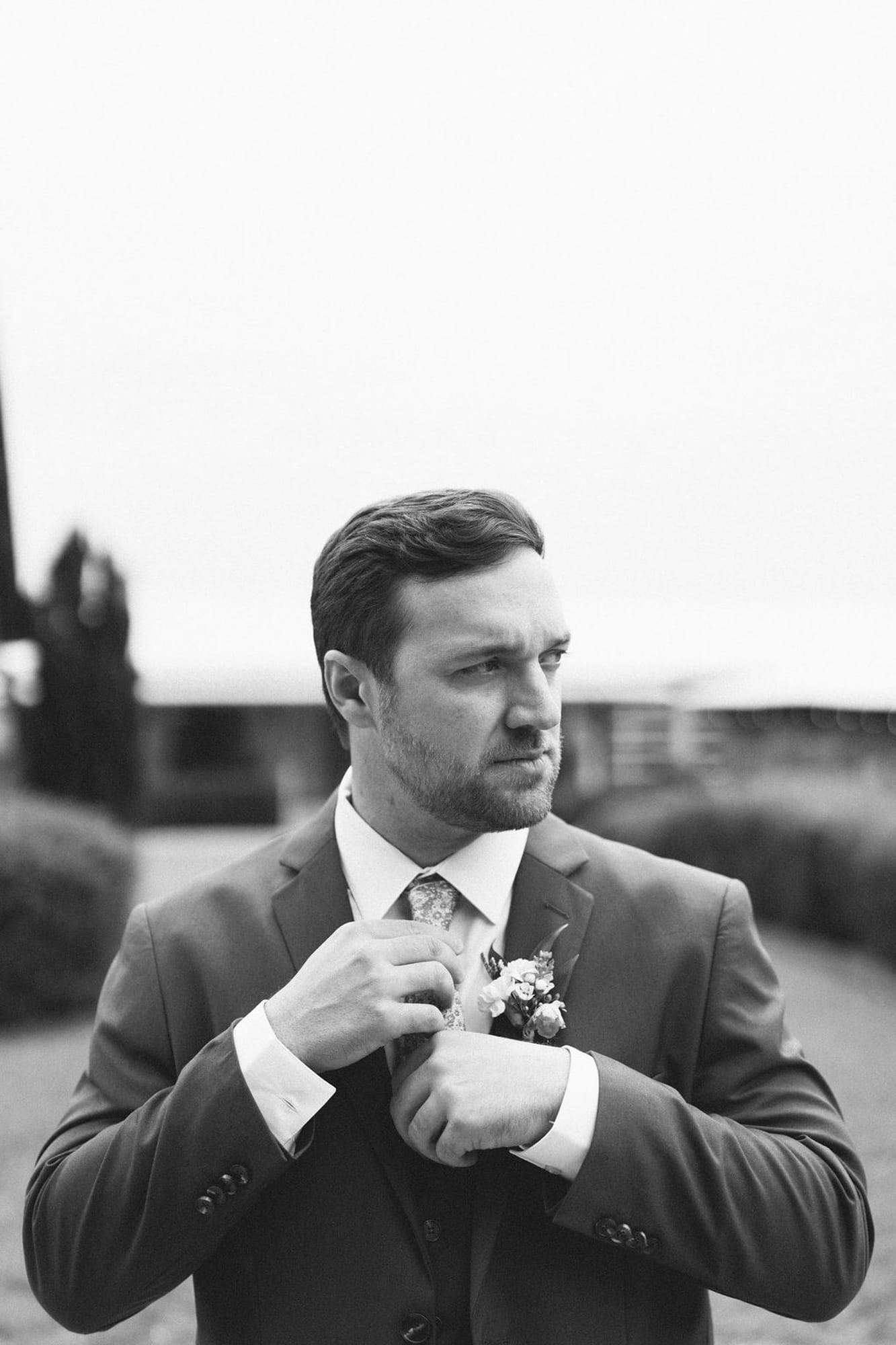Groom adjusting his boutonniere outdoors, black and white portrait