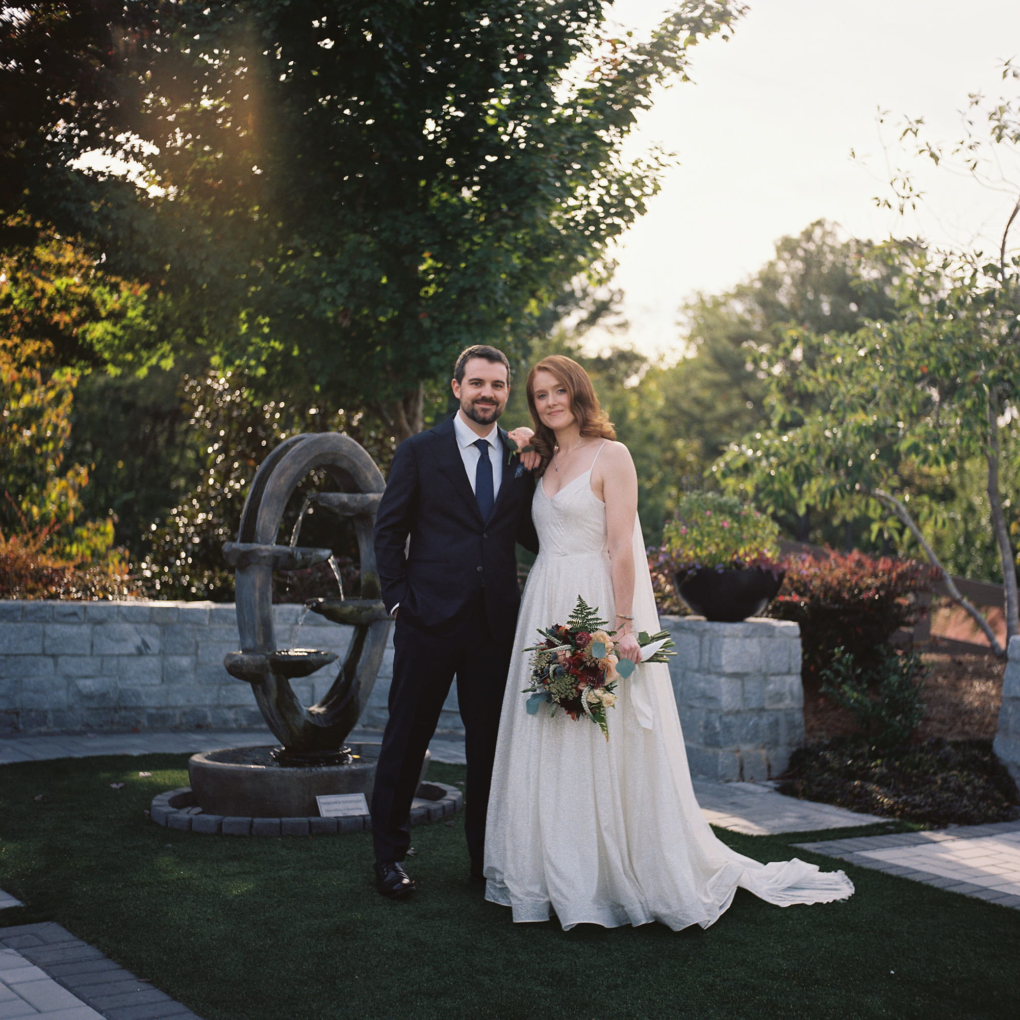 Bride and groom portrait at sunset in a garden with a stone fountain