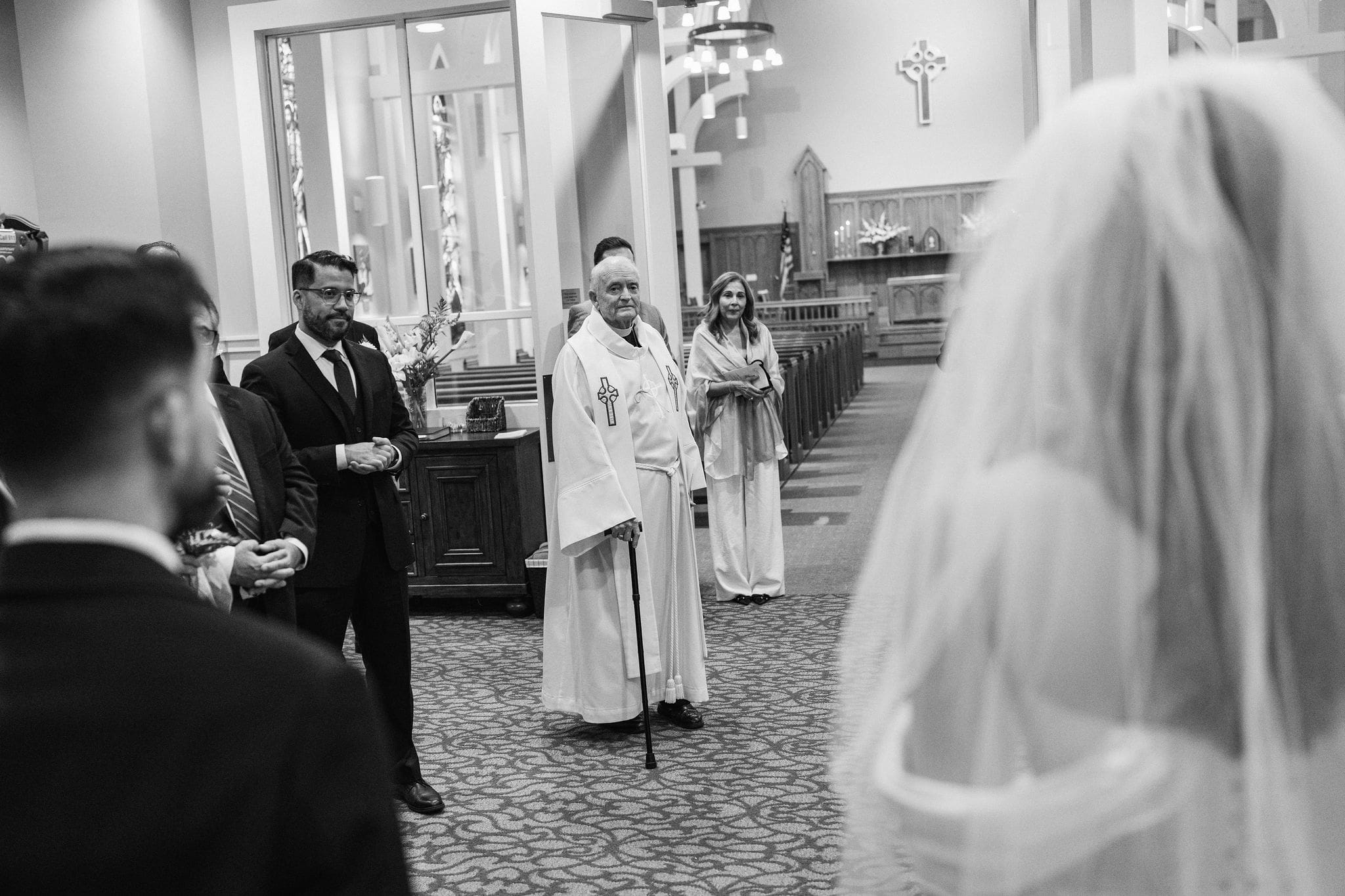 Bride walking down the church aisle toward the officiant, black and white
