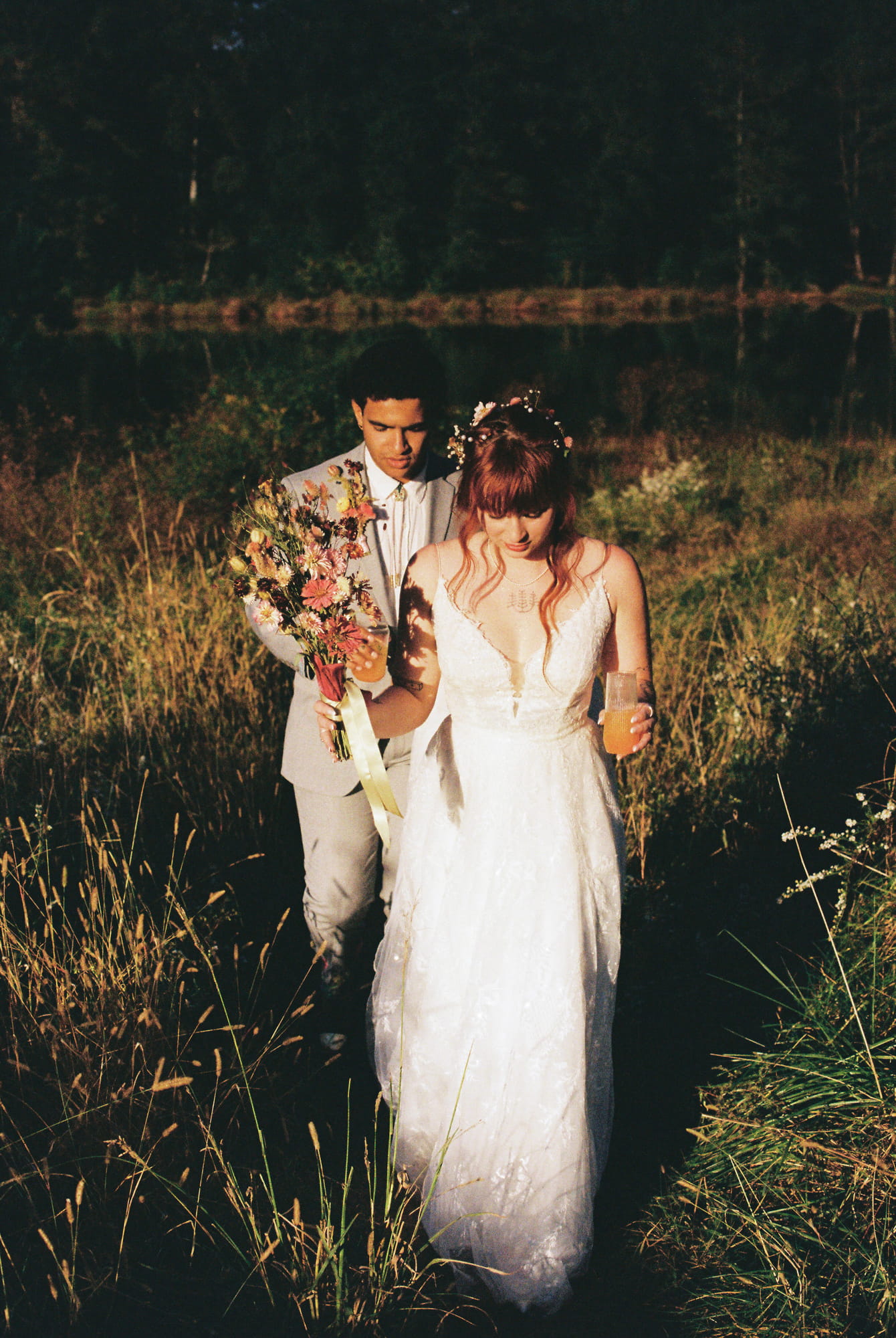 Bride and groom walking through tall golden grass at sunset, bride wearing flower crown