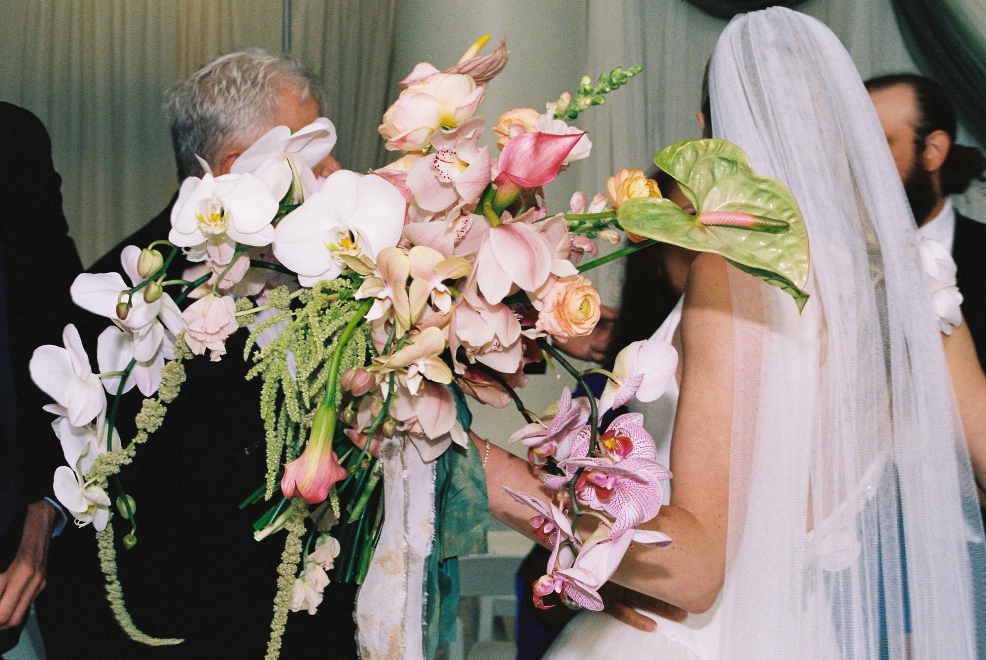 Father embracing bride through an oversized orchid and tropical flower bouquet