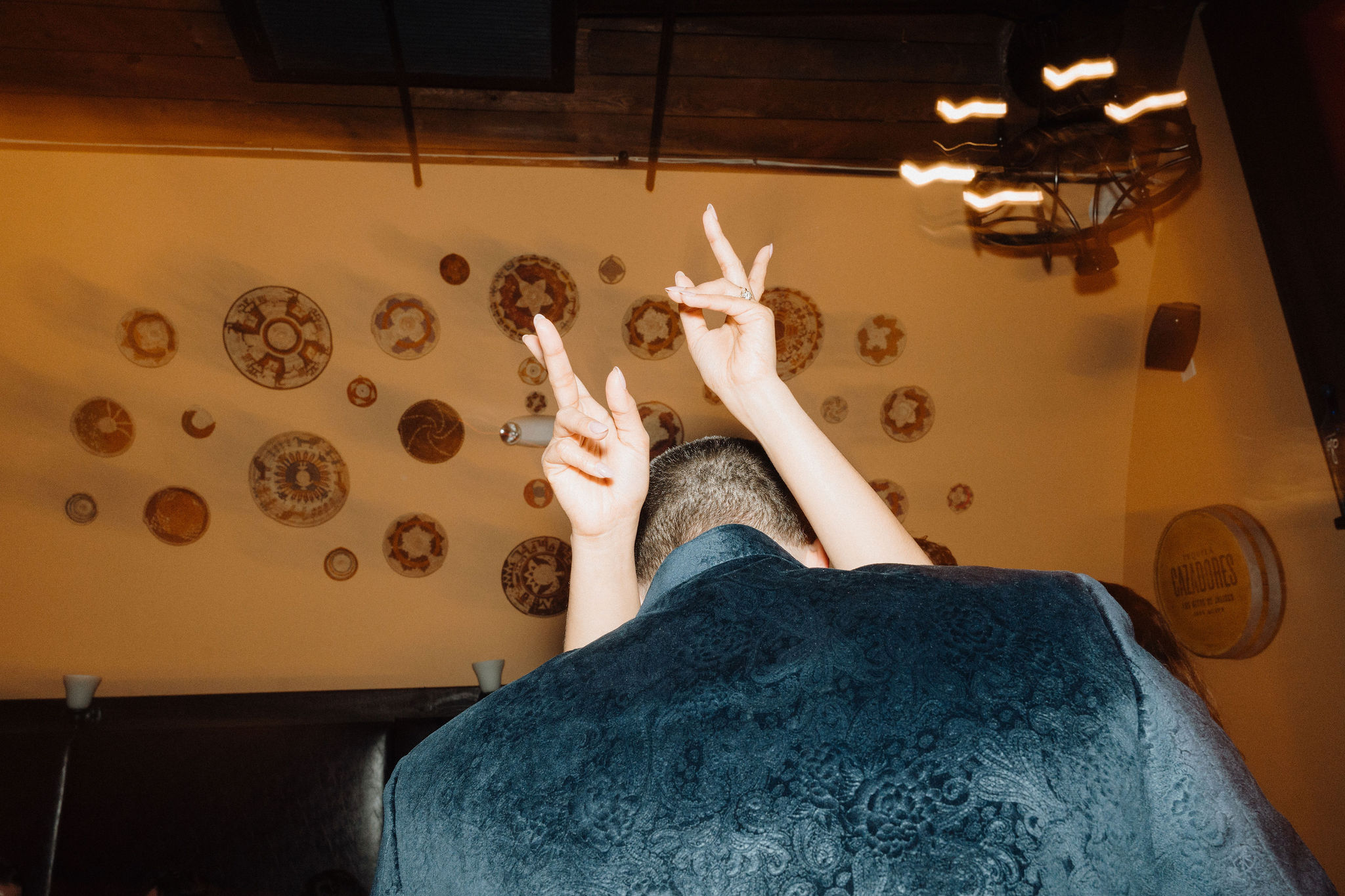 Overhead view of couple at a reception, bride flashing a peace sign with rings visible