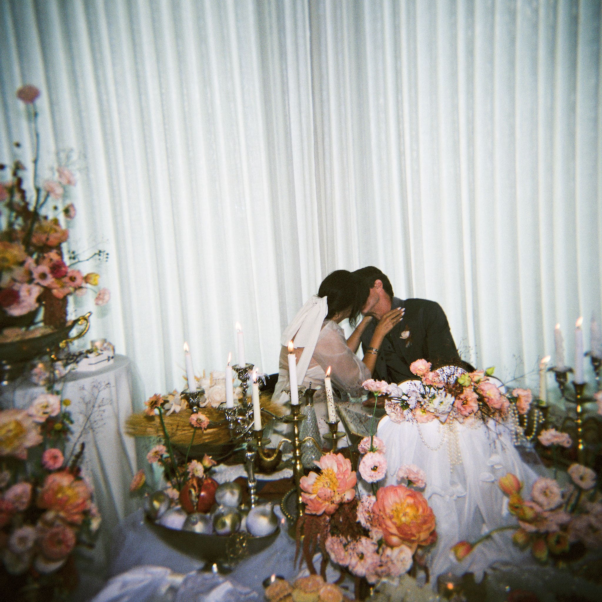 Bride and groom stealing a kiss at their sweetheart table surrounded by candlelight and lush floral arrangements