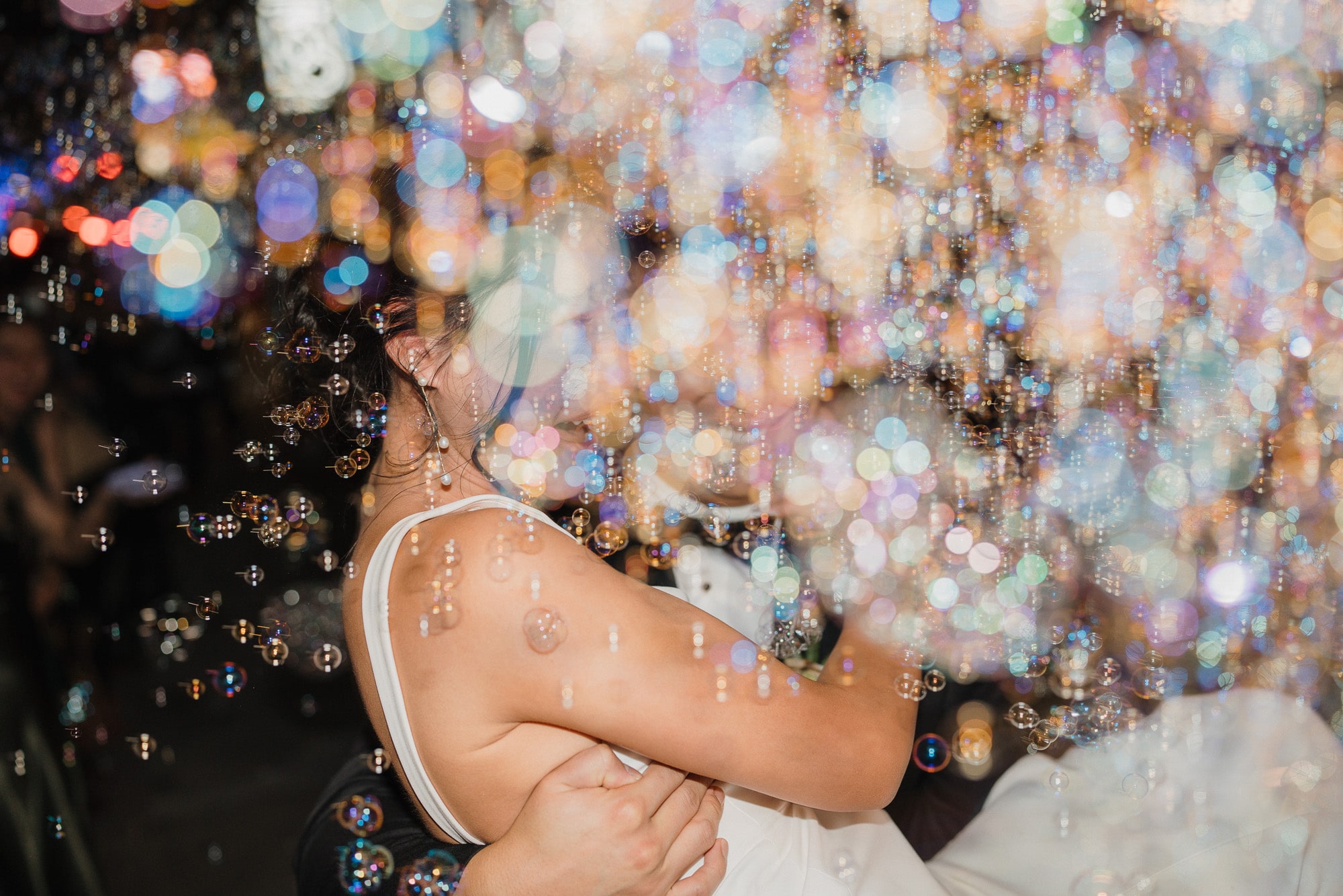 Bride and groom embracing in a shower of colorful bubbles at night