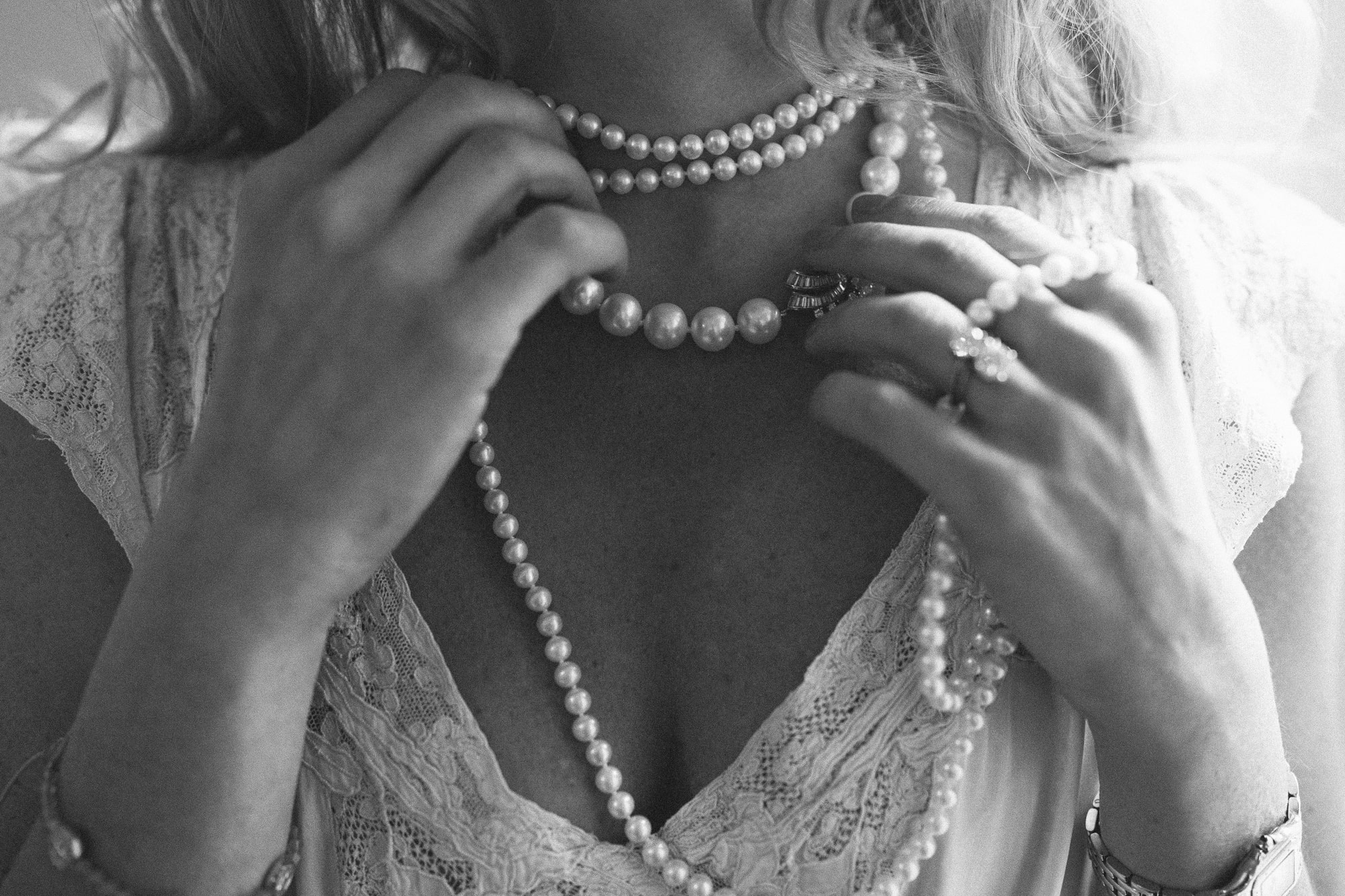 Bride adjusting layered pearl necklaces, black and white close-up detail shot